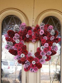 a heart shaped wreath made out of pine cones on a front door with two large windows