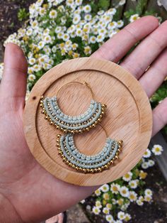 a hand holding a wooden hoop with beaded earrings on it and flowers in the background