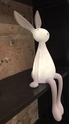 a white rabbit lamp sitting on top of a wooden shelf next to a brick wall