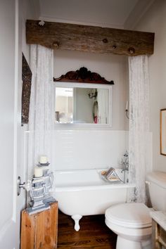 a white bath tub sitting next to a toilet in a bathroom under a wooden beam