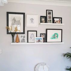 a wall with pictures, frames and flowers on it in a room that has white walls