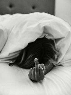 a woman laying in bed with her head on the pillow and pointing to the side