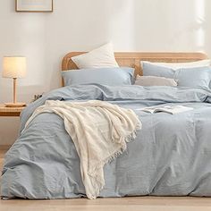 a bed with blue sheets and pillows in a room next to a lamp on the floor