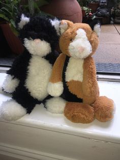 two stuffed cats sitting on top of a window sill