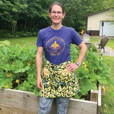 a woman wearing an apron standing in front of a garden filled with plants and vegetables