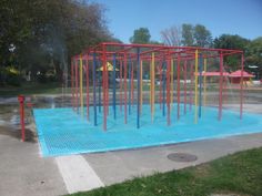 an outdoor play area with blue water and red metal structures on the ground, surrounded by green grass