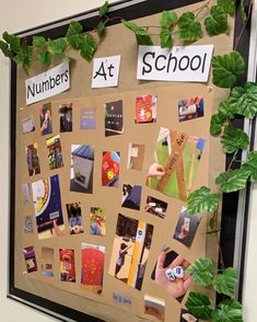 a bulletin board covered in pictures and magnets with green leaves on the wall next to it