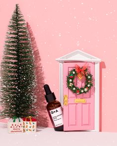 a bottle of argan oil next to a pink door and christmas tree with presents