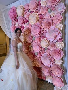 a bride standing in front of a large flower wall with pink flowers on it's side