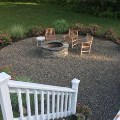 a fire pit surrounded by wooden chairs and flowers in the back yard with gravel around it