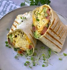 a burrito is cut in half and sitting on a plate with green garnishes