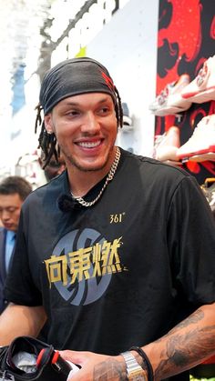 a man with dreadlocks smiles at the camera while wearing a black t - shirt