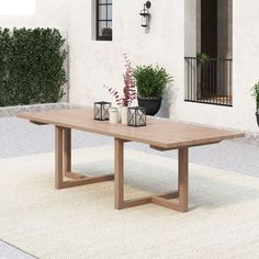 a wooden table sitting in front of a white building with potted plants on it