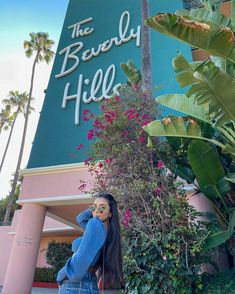 a woman is standing in front of the beverly hills sign and talking on her cell phone