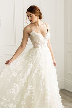 a woman in a white wedding dress with flowers on the skirt is standing and looking down