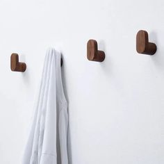 three wooden hooks hang on the wall next to a white robe hanging from it's hooks