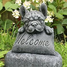 a statue of a dog with the word welcome on it's pillow in front of some flowers