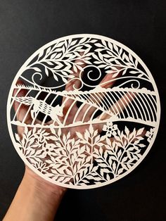 a hand holding a circular cutout with birds and flowers on it's side