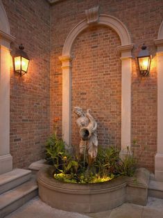 a fountain in front of a brick building with two lights on each side and plants growing out of it