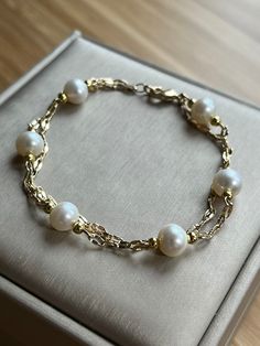 This delicate bracelet showcases a duo of 14k gold-plated chains, gracefully intertwined to form a double-layered embrace around the wrist. Adorned with six lustrous freshwater pearls, each sized at 7-8mm, the bracelet exudes a serene elegance. The pearls are evenly spaced, creating a harmonious balance with the shimmering gold links. This piece merges the timeless appeal of pearls with the modern finesse of layered chains, making it a versatile accessory for both casual and formal attire. Layered Chains, Freshwater Pearl Bracelet, Gold Plated Chains, Adjustable Bracelet, Pearl Bracelet, Delicate Bracelet, Arm Band, Fresh Water, Freshwater Pearls