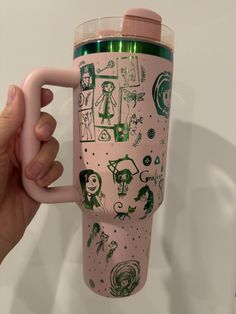 a person holding a pink coffee cup with pictures on it and a light green lid