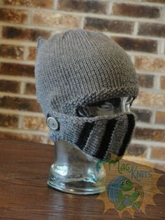 a gray knitted hat on top of a glass cup with a button in the middle