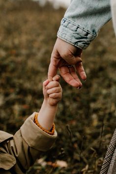 a person holding the hand of a child's hand while standing in a field