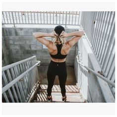 a woman in black sports bra top and leggings standing on stairs with her back to the camera