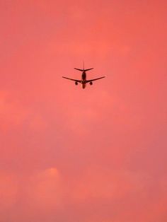 an airplane is flying in the pink sky