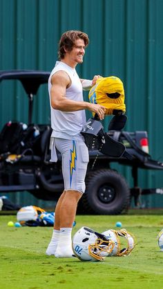 a man holding a football helmet and glove on top of a field next to a soccer ball