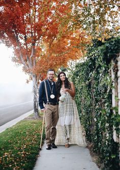 a man and woman standing next to each other on a sidewalk with trees in the background