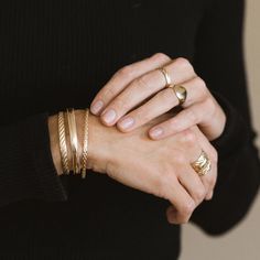 a woman's hands with gold rings and bracelets on her wrist, wearing a black sweater