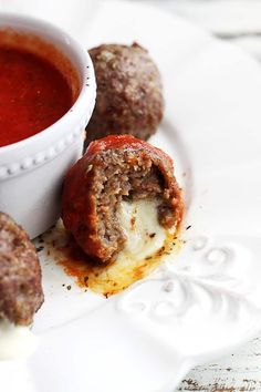 some meatballs are on a white plate with a bowl of tomato soup in the background