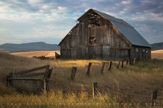 an old barn sits in the middle of a field