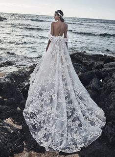 a woman standing on rocks near the ocean wearing a wedding dress with an open back