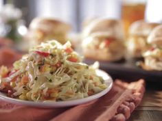 a white plate topped with coleslaw next to two plates of hamburger patties