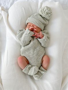 a baby in a knitted outfit laying on top of a white blanket