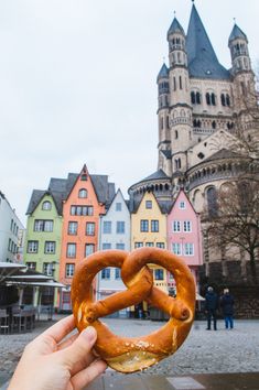 a person holding up a pretzel in front of some colorful buildings on a cloudy day