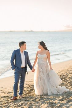 a bride and groom holding hands walking on the beach at sunset in front of the ocean