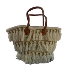 Experience the perfect blend of traditional craftsmanship and contemporary style with our handcrafted Moroccan raffia bag. This stunning piece features intricate woven patterns and eye-catching fringes that showcase the exceptional skill of Moroccan artisans. Adorned with three layers of elegant fringes, it adds a playful yet sophisticated touch to any outfit. The durable leather handles ensure comfortable carrying, making it ideal for both daily use and special occasions. Each bag is a unique c Bohemian Bucket Tote Bag With Tassels, Bohemian Bucket Bag Tote With Tassels, Bohemian Tote Bucket Bag With Tassels, White Bohemian Bucket Beach Bag, Bohemian White Bucket Beach Bag, Bohemian Bucket Bag With Tassels For Daily Use, Bohemian Bucket Bag With Braided Handles, Bohemian Straw Shopping Bag, Bohemian Straw Bag For Shopping