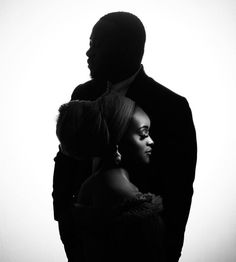 a man and woman standing next to each other in front of a white wall,