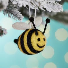 a small yellow and black bee ornament hanging from a christmas tree with snow on it