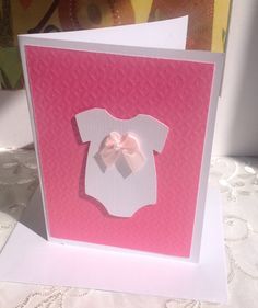 a pink and white card with a baby's bodysuit on it, sitting on a table