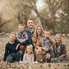 a family posing for a photo in the woods with leaves on the ground and trees behind them