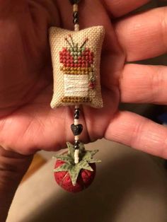 someone is holding a small needle - embroidered strawberry keychain that has been made to look like a pillow