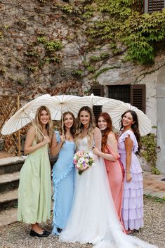 four bridesmaids pose with their umbrellas in front of an old stone building