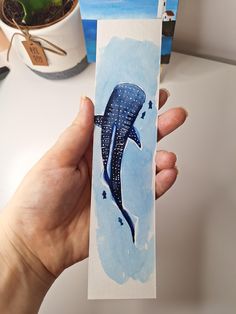 a painting of a blue whale is being held in front of a cup and plant