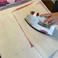 a woman ironing fabric with a pink and white electric iron on top of it