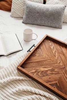 a wooden tray sitting on top of a bed next to an open book and coffee cup