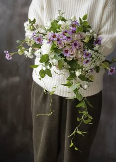 a person holding a bouquet of flowers in their hands and wearing a sweater over them